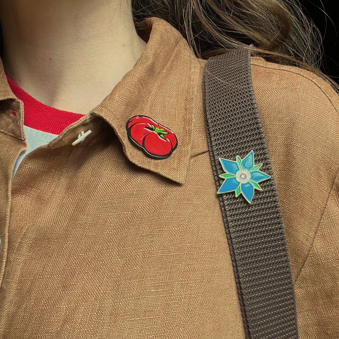 Mikado Tomato enamel pin from a gift shop, featuring a colorful tomato design on a person&