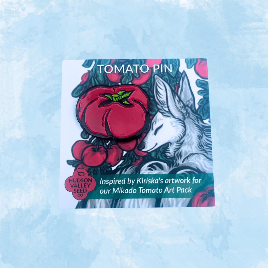 Pink and red Mikado Tomato enamel pin with detailed design, displayed alongside an art card, from a gift shop collection.