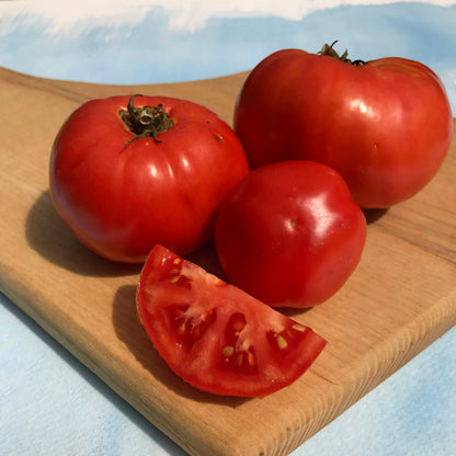 Fresh Cosmonaut Volkov tomato from Hudson Valley Seed Co., showcasing vibrant red, round vegetable on a vendor stand.