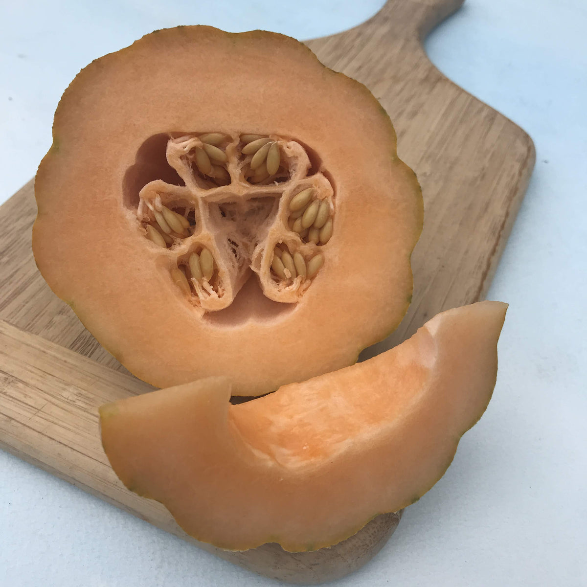 Minnesota Mini Melon vegetable from Hudson Valley Seed Co., small round melon with green striped skin and orange flesh.